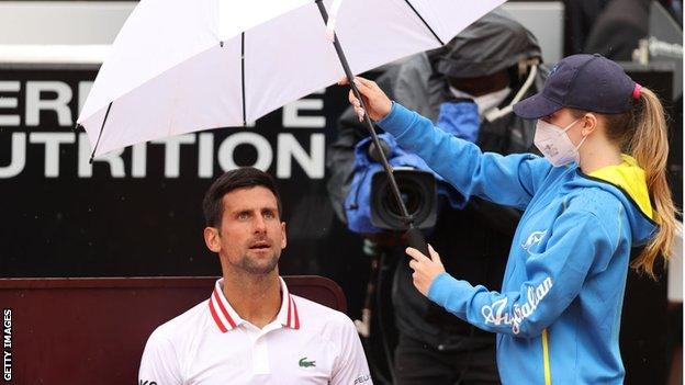 Novak Djokovic sits under an umbrella